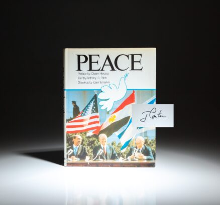 First edition of Peace, a photographic history of the Camp David Accords, with text by Anthony S. Pitch and a preface by Chaim Herzog. Signed by President Jimmy Carter on the half-title.